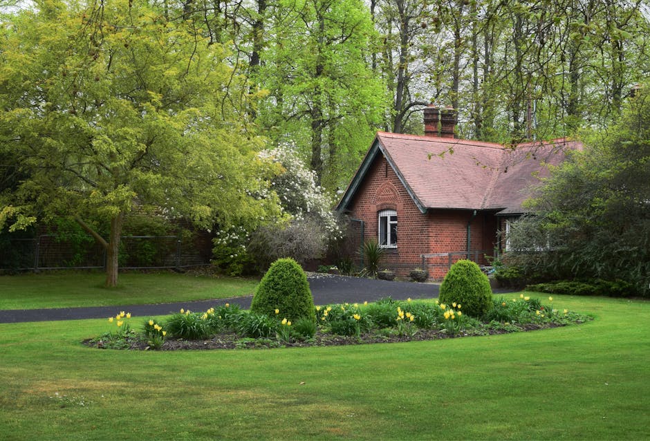 A landscaped garden featuring a paved brick pathway winding through lush greenery, including large decorative stone planters filled with green plants, ferns, and flowering foliage. The pathway is bord