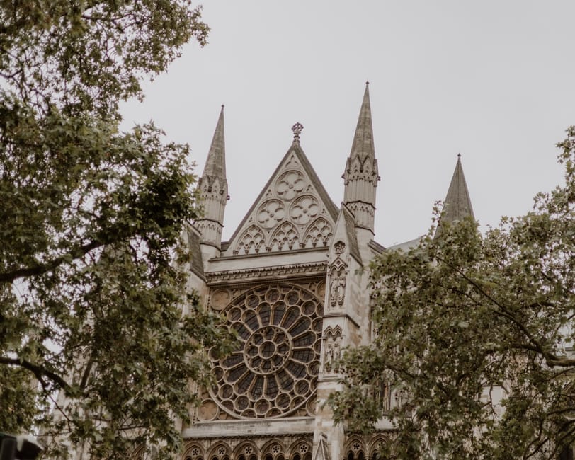 The image features the façade of Westminster Abbey, showcasing its intricate Gothic architectural design with pointed spires, ornate stone carvings, and a large circular stained glass window at the ce