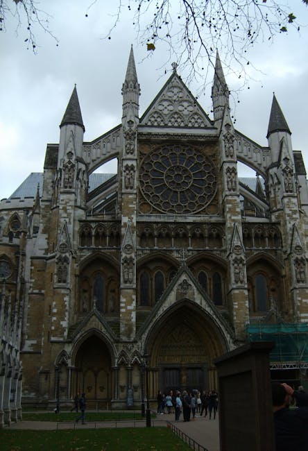 The image features the façade of Westminster Abbey, showcasing its intricate Gothic architectural design with pointed spires, ornate stone carvings, and a large circular stained glass window at the ce